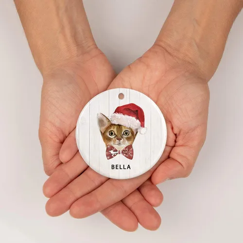 Vista 4 de Andaz Press Adorno redondo personalizado de cerámica para árbol de Navidad, abisinio, corona de acebo, sombrero de Papá Noel, con gráfico de gato