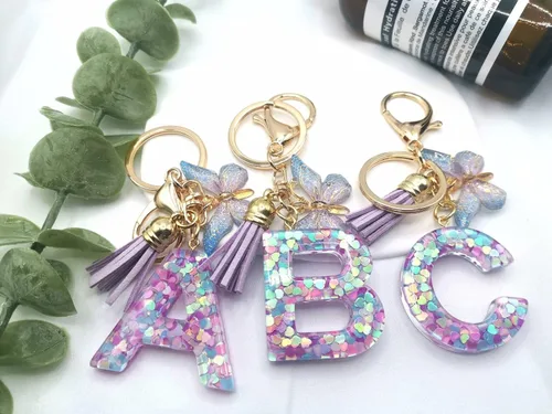 Vista 2 de Llavero con letra inicial del alfabeto de resina morada, azul, rosa, borla, mariposa, llavero para bolso, cartera, bolso, llaves del coche