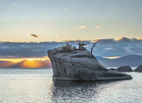 Vista 2 de Noah Jigsaw Puzzle USA, Nevada, condado de Washoe, lago Tahoe. Bonsai roca frente a la puesta de sol frijoles brillando bajo una capa de nubes sobre