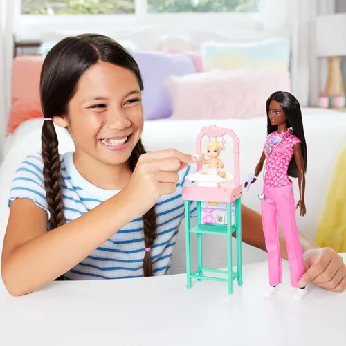 Vista 2 de Barbie Baby Doctor Playset con muñeca morena con ropa quirúrgica rosa, muñeca de bebé, muebles y accesorios