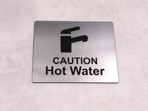 Vista 2 de Caution Hot Water, letrero para fregadero con adhesivo en la parte posterior, plateado metálico grabado en negro con símbolo de icono universal